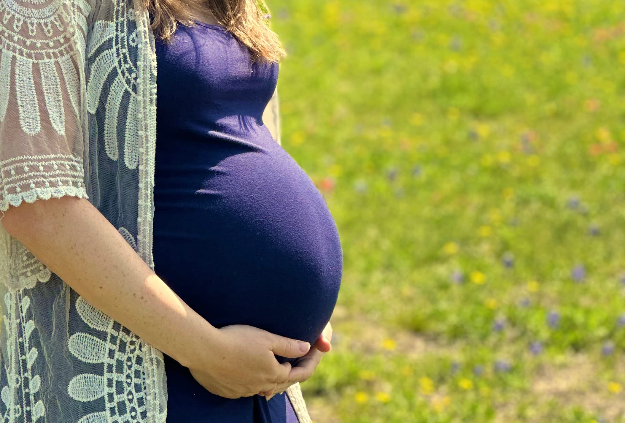 A pregnant woman cradling her belly in a sunlit wildflower field